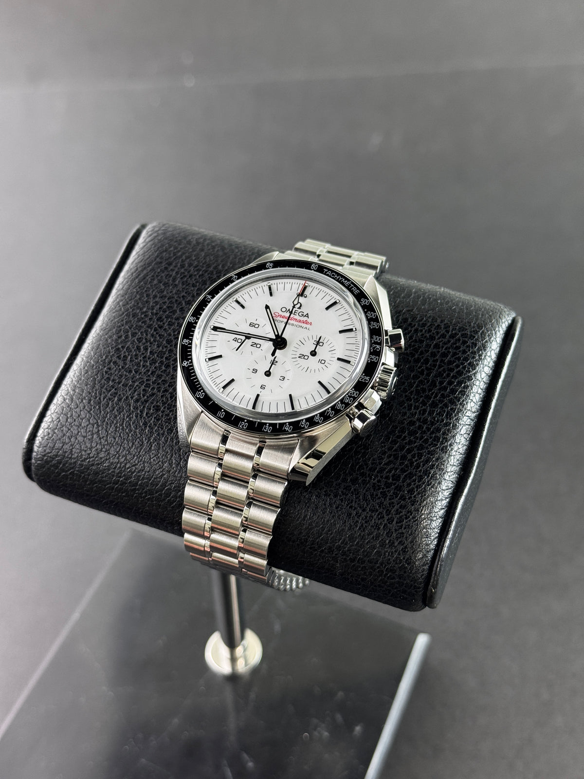 Omega Speedmaster Professional Moonwatch à cadran blanc sur bracelet en acier, posée sur un coussin en cuir noir